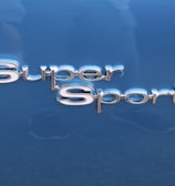 The image features the words 'Super Sport' in shiny, metallic lettering. The background is a smooth, glossy blue surface, likely part of a vehicle.