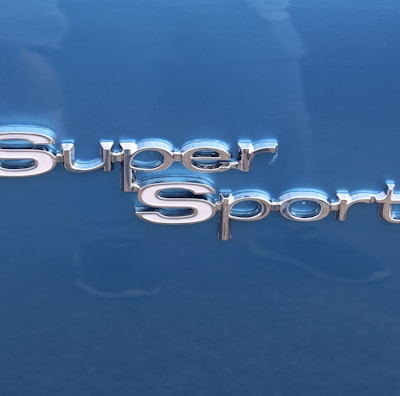 The image features the words 'Super Sport' in shiny, metallic lettering. The background is a smooth, glossy blue surface, likely part of a vehicle.